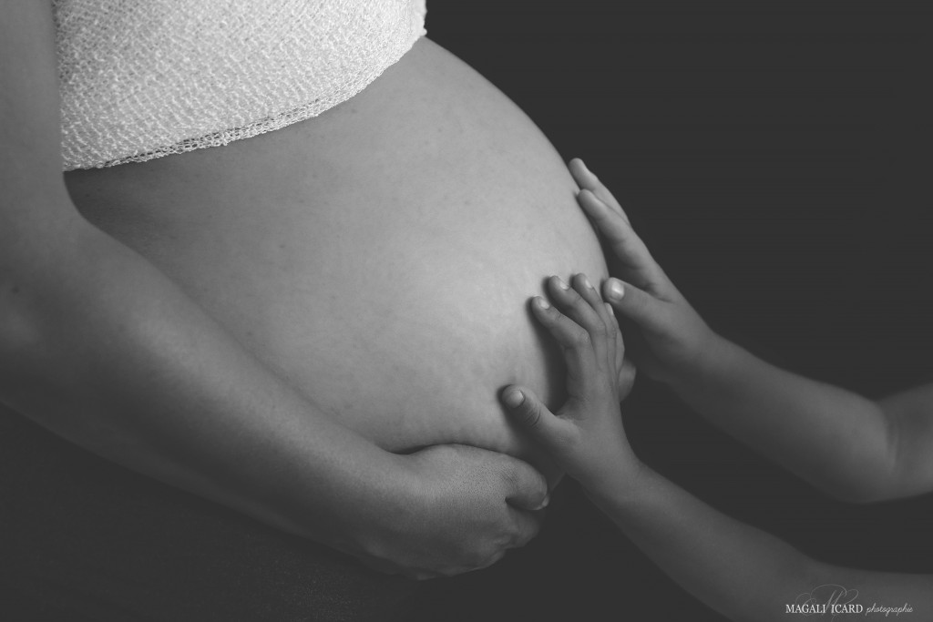 Photo de grossesse en noir et blanc avec les mains des enfants